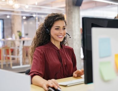 Customer support phone operator working at computer. Happy call center agent working on support hotline in office. Smiling call center agent in conversation with customer over headset.